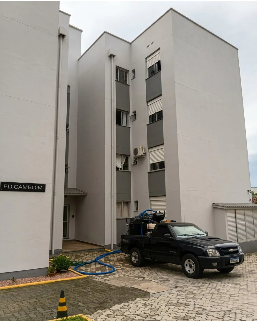 Picape preta com unidade de hidrojateamento e mangueiras em condomínio